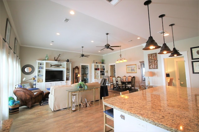 kitchen featuring light stone counters, light hardwood / wood-style flooring, hanging light fixtures, and ornamental molding