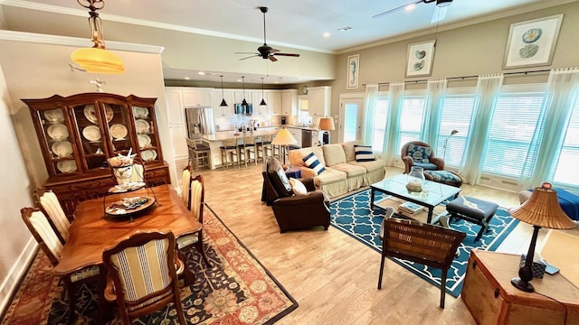 living room with ceiling fan, a towering ceiling, ornamental molding, and light wood-type flooring