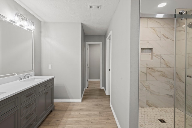 6425 Adams Blvd, Groves, TX 77619 - full bathroom featuring double vanity, a tile shower, wood finished floors, and a textured ceiling