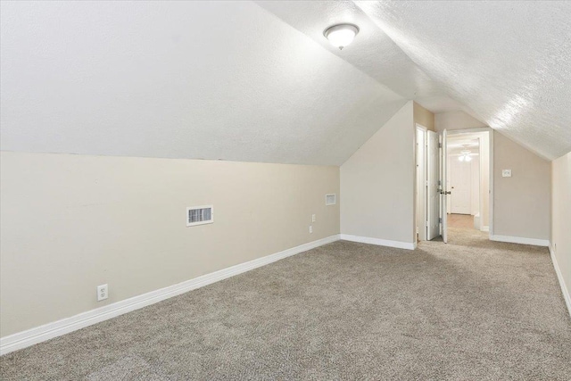 additional living space featuring light colored carpet, a textured ceiling, and vaulted ceiling