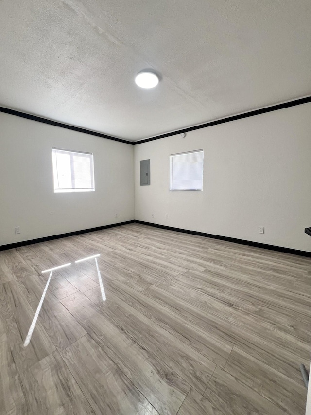 unfurnished room with electric panel, crown molding, a textured ceiling, and light wood-type flooring