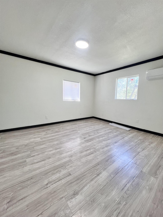 unfurnished room featuring a textured ceiling, light wood-type flooring, an AC wall unit, and crown molding