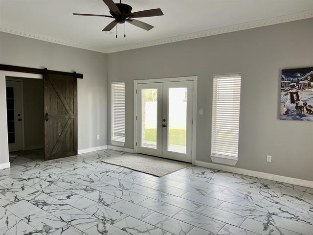 7600 Oakmont Dr, Port Arthur, TX 77642 - empty room featuring marble finish flooring, a barn door, ceiling fan, french doors, and baseboards