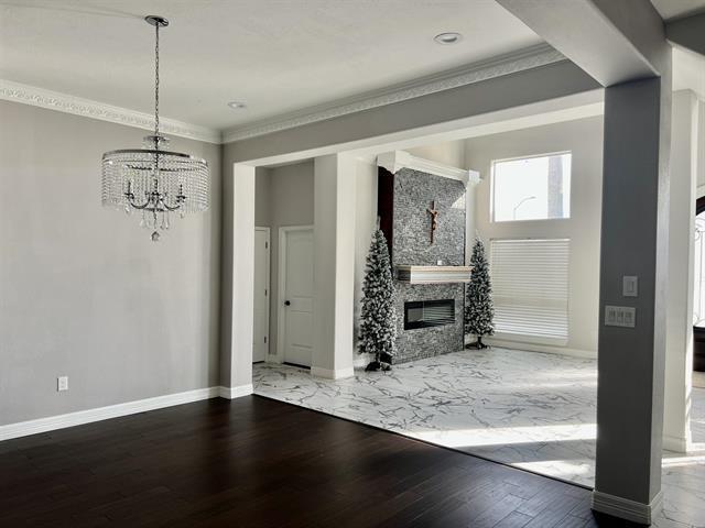 7600 Oakmont Dr, Port Arthur, TX 77642 - unfurnished living room with a chandelier, wood finished floors, baseboards, a glass covered fireplace, and ornamental molding