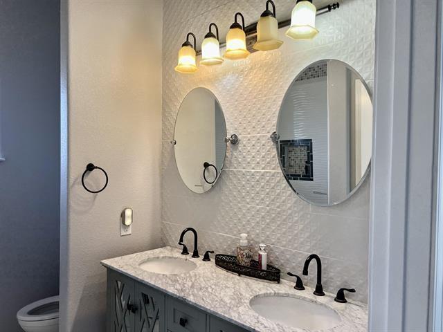 7600 Oakmont Dr, Port Arthur, TX 77642 - bathroom with double vanity, decorative backsplash, and toilet