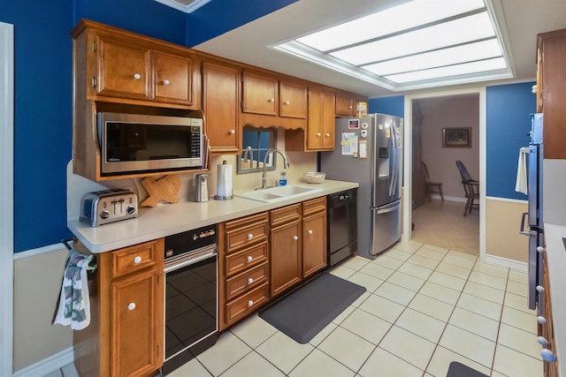 kitchen featuring brown cabinets, light countertops, light tile patterned floors, a sink, and black appliances