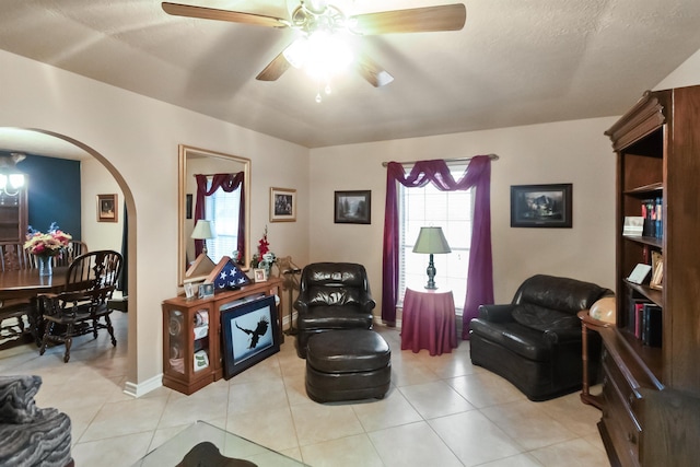 living area with light tile patterned floors, a wealth of natural light, arched walkways, and ceiling fan