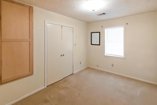 unfurnished bedroom featuring light carpet, a closet, and a textured ceiling