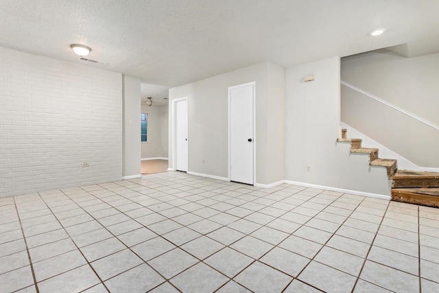 tiled empty room with a textured ceiling and brick wall