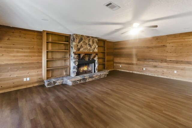 unfurnished living room with a textured ceiling, a stone fireplace, wood walls, and dark hardwood / wood-style floors