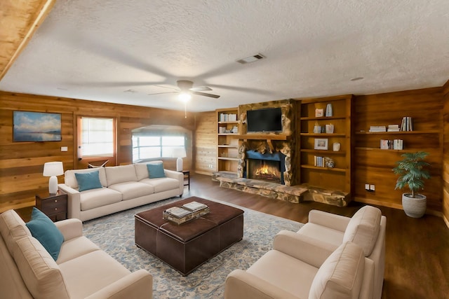 living room featuring wood walls, dark wood-type flooring, ceiling fan, a textured ceiling, and a fireplace