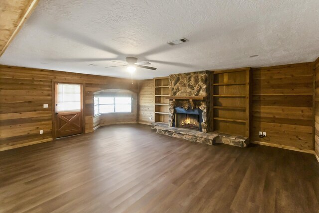 unfurnished living room with a fireplace, dark hardwood / wood-style floors, ceiling fan, and wood walls