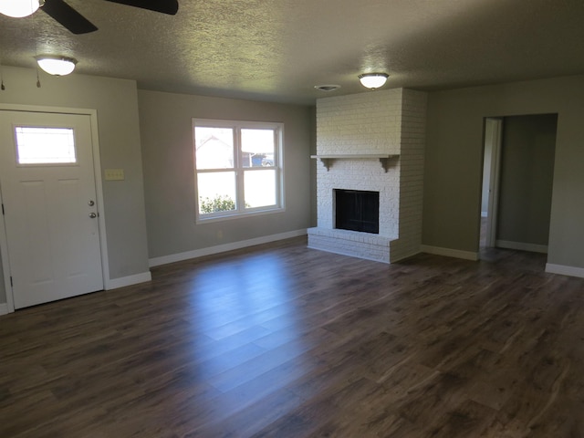 unfurnished living room featuring dark wood-type flooring, a brick fireplace, plenty of natural light, and a textured ceiling