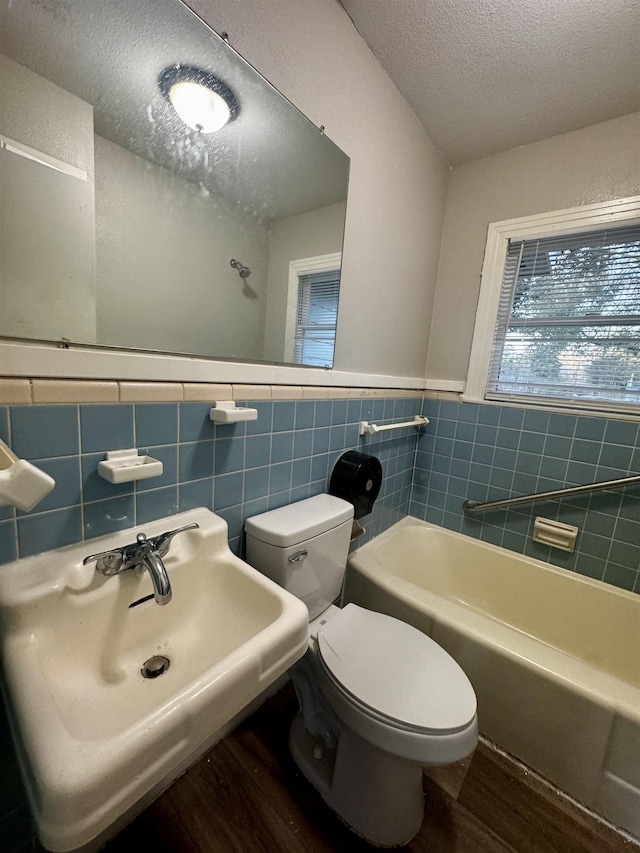 bathroom featuring tile walls, hardwood / wood-style floors, a textured ceiling, toilet, and a bathing tub