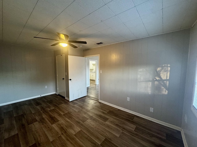 unfurnished room with dark wood-type flooring, wooden walls, and ceiling fan