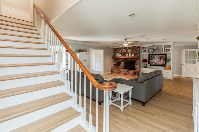 living room featuring ceiling fan, light wood-type flooring, crown molding, and a brick fireplace