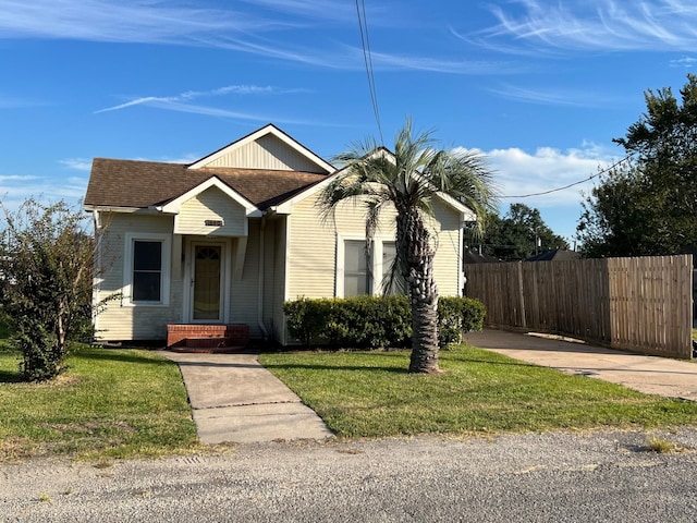 view of front of house with a shingled roof, a front yard, and fence