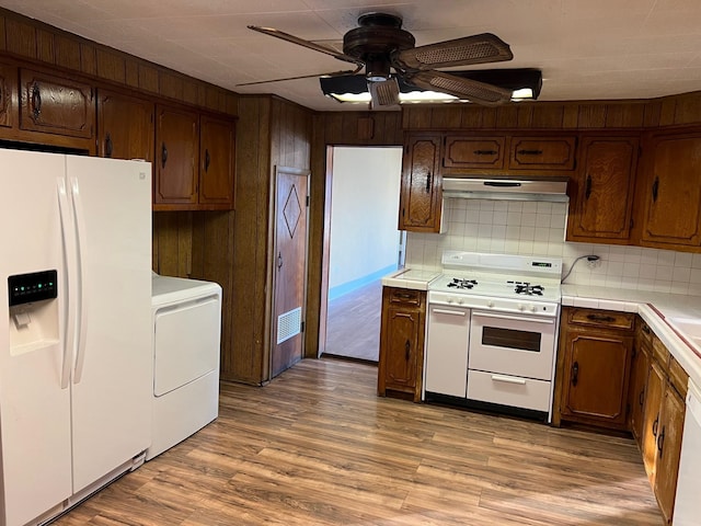 kitchen with tile countertops, light wood finished floors, washer / dryer, white appliances, and under cabinet range hood