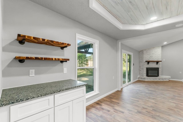 kitchen featuring a fireplace, light hardwood / wood-style flooring, dark stone countertops, white cabinets, and lofted ceiling