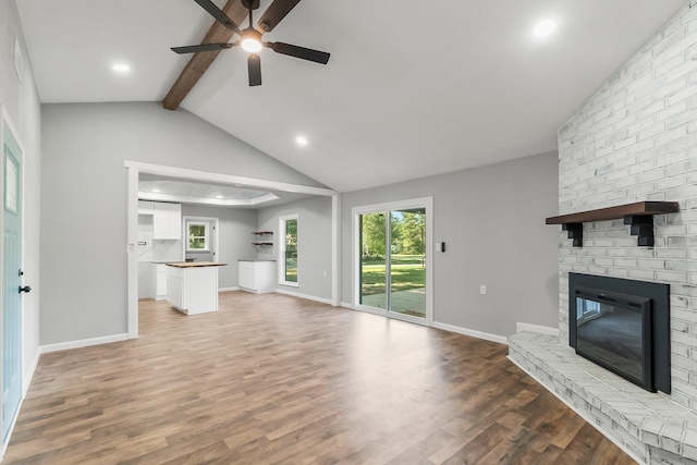 unfurnished living room featuring hardwood / wood-style floors, vaulted ceiling with beams, ceiling fan, and a fireplace