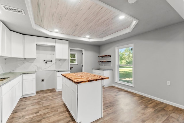 kitchen with a raised ceiling, backsplash, butcher block countertops, and white cabinets