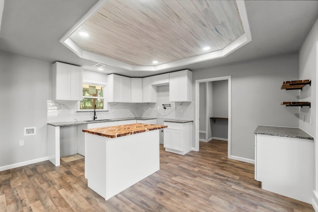 kitchen with a tray ceiling, butcher block counters, and white cabinetry