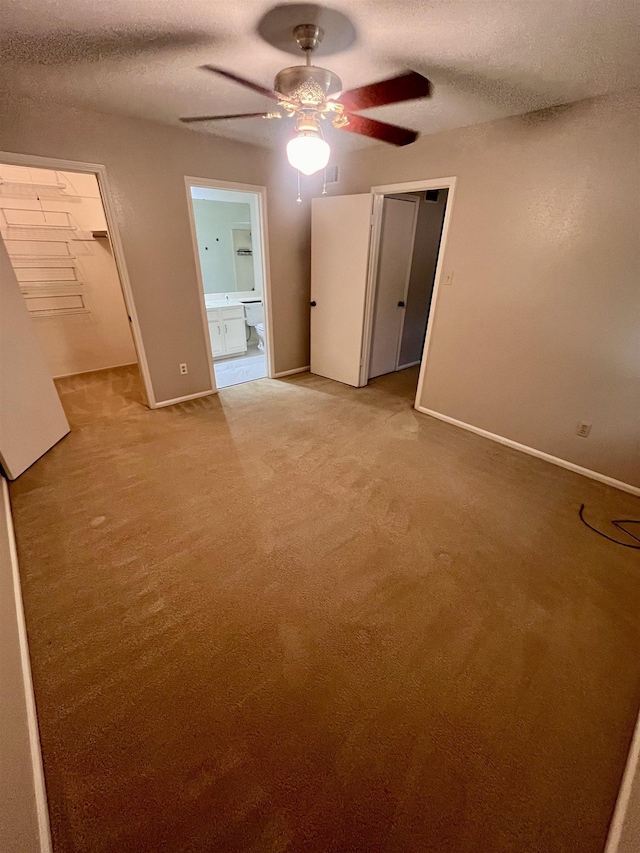 unfurnished bedroom featuring a textured ceiling, baseboards, connected bathroom, light colored carpet, and a closet