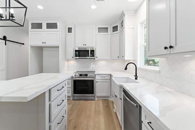 kitchen with stainless steel appliances, sink, decorative light fixtures, a chandelier, and white cabinetry