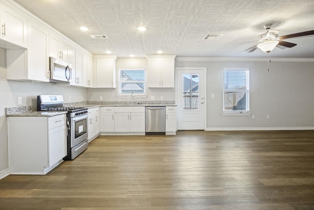 kitchen featuring light stone countertops, wood finished floors, visible vents, appliances with stainless steel finishes, and white cabinetry