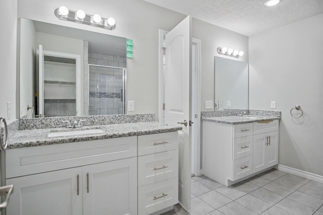 bathroom with tile patterned flooring, two vanities, a stall shower, a textured ceiling, and a sink