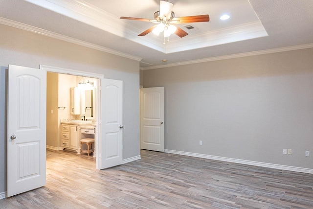 unfurnished bedroom with ceiling fan, crown molding, ensuite bathroom, and a tray ceiling