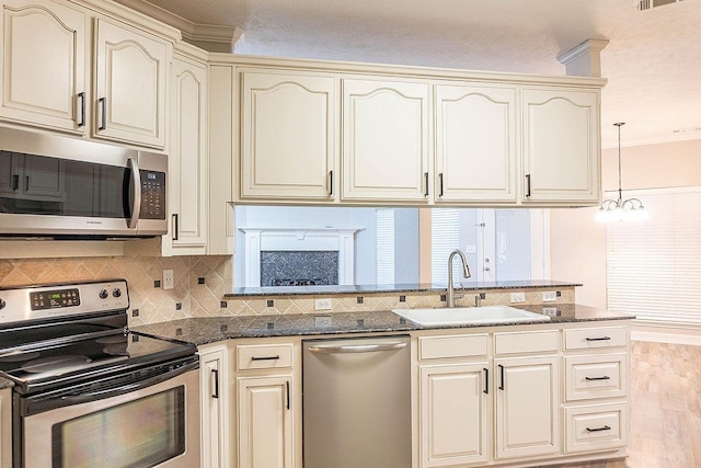 kitchen featuring stainless steel appliances, sink, cream cabinets, an inviting chandelier, and hanging light fixtures