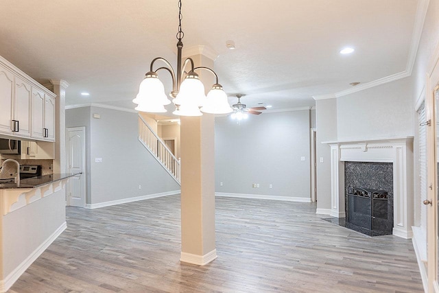 unfurnished living room featuring a fireplace, ceiling fan with notable chandelier, light hardwood / wood-style floors, and ornamental molding