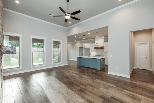 unfurnished living room with ceiling fan, sink, a towering ceiling, and crown molding