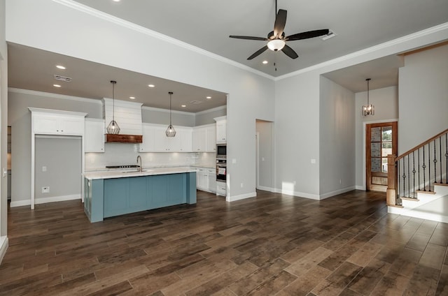 kitchen with pendant lighting, wall oven, white cabinetry, and an island with sink