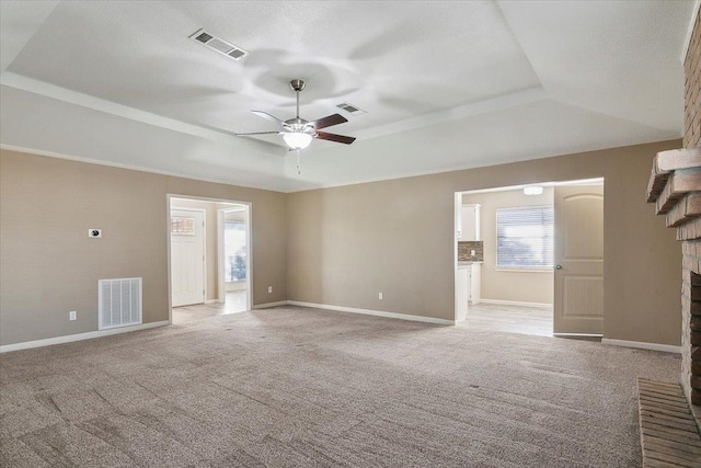 unfurnished living room with plenty of natural light, ceiling fan, a raised ceiling, and a brick fireplace