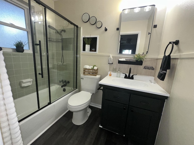 full bathroom featuring wood finished floors, a wainscoted wall, vanity, toilet, and shower / bath combination with glass door