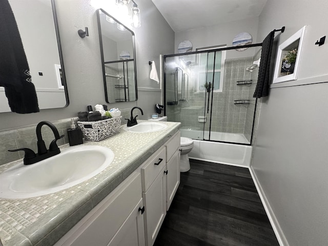 full bath featuring toilet, combined bath / shower with glass door, a sink, and wood finished floors