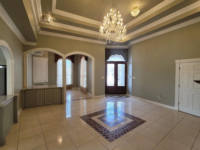 foyer entrance featuring a tray ceiling, french doors, arched walkways, light tile patterned flooring, and a chandelier