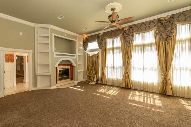 unfurnished living room featuring built in shelves, crown molding, carpet, a glass covered fireplace, and a ceiling fan