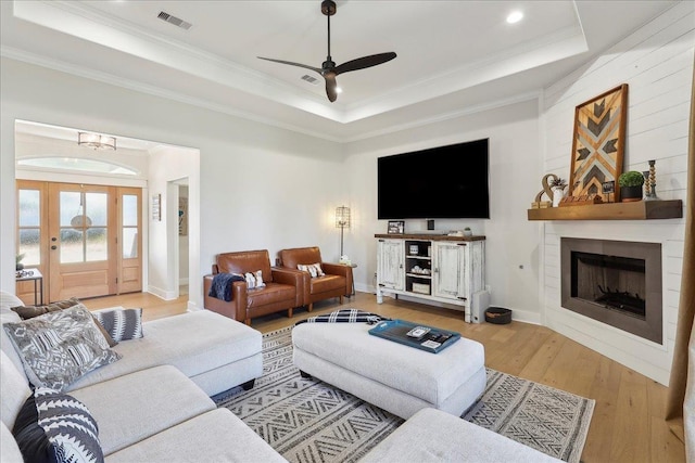 living area featuring visible vents, a large fireplace, ornamental molding, hardwood / wood-style floors, and a raised ceiling