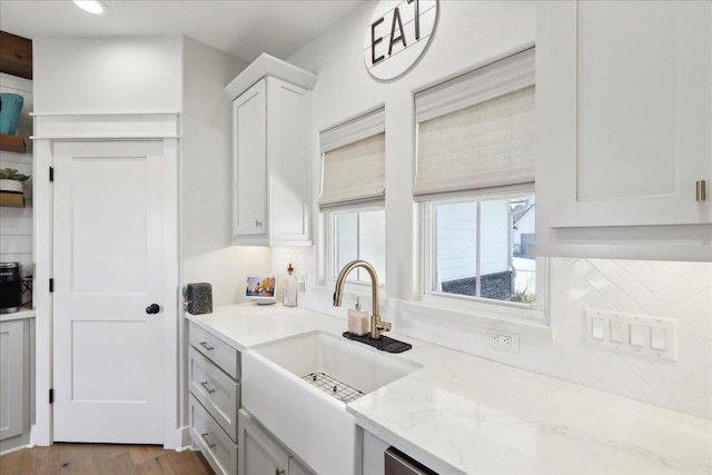 kitchen featuring a sink, backsplash, wood finished floors, white cabinetry, and light stone countertops