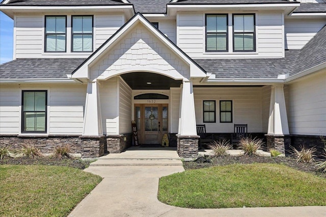 entrance to property featuring stone siding, french doors, covered porch, and roof with shingles