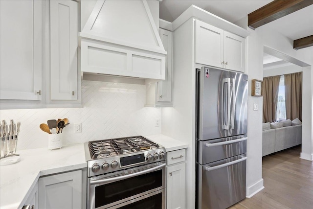 kitchen with beam ceiling, custom range hood, tasteful backsplash, white cabinetry, and appliances with stainless steel finishes