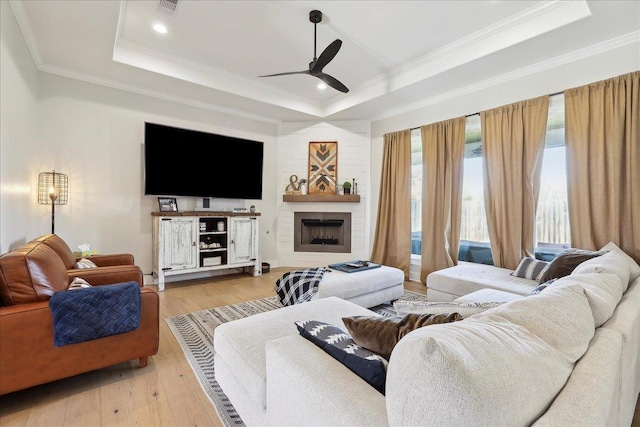 living room with light wood finished floors, a raised ceiling, a ceiling fan, and ornamental molding