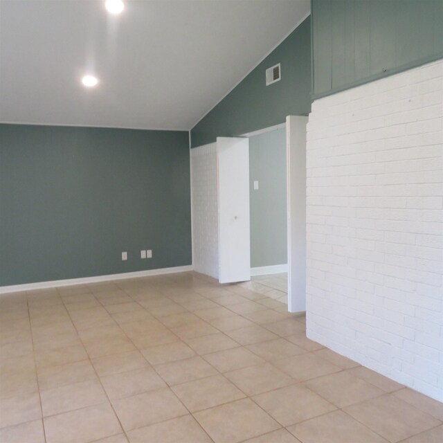 unfurnished room featuring visible vents, vaulted ceiling, brick wall, and light tile patterned floors