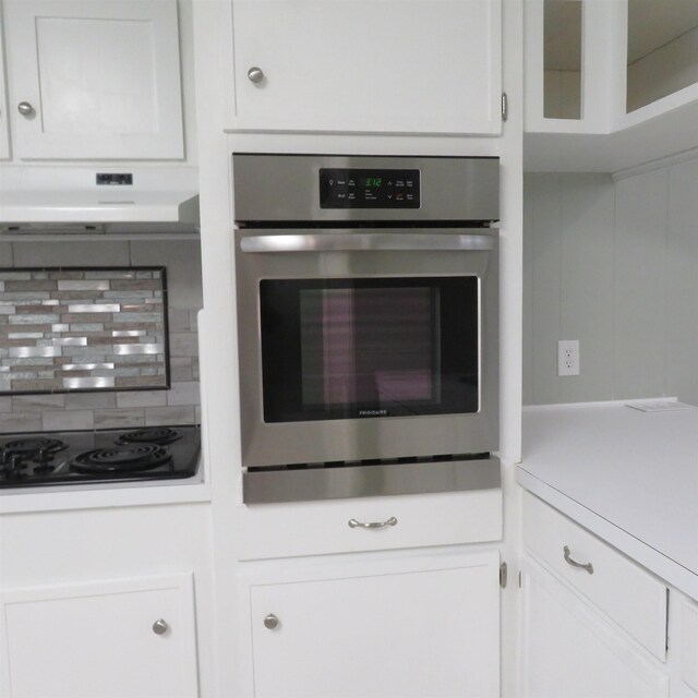 kitchen with white cabinets, decorative backsplash, black electric cooktop, under cabinet range hood, and stainless steel oven