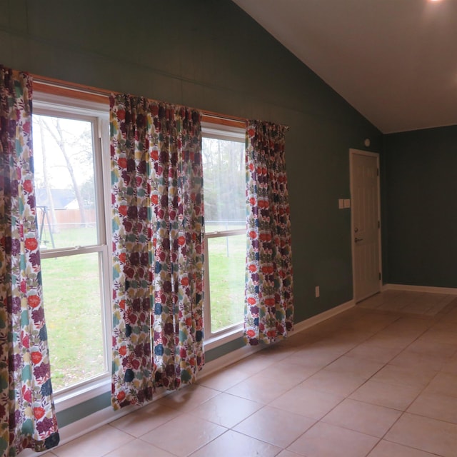 empty room featuring baseboards, vaulted ceiling, and light tile patterned flooring