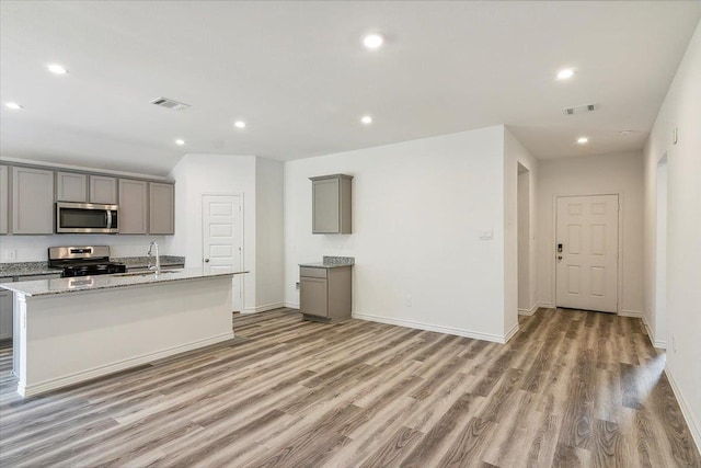 kitchen featuring gray cabinets, light stone countertops, a kitchen island with sink, and appliances with stainless steel finishes