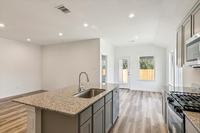 kitchen with sink, stainless steel appliances, light stone counters, a kitchen island with sink, and light wood-type flooring